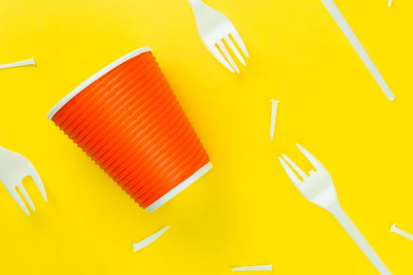 Pattern of broken plastic forks, and plastic cup on a yellow background.
