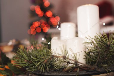 Beyaz mumlardan, kozalaklı mandallardan ve hediyelerden oluşan bir masanın üzerindeki Noel dekoru. Firavun Noel çelengi