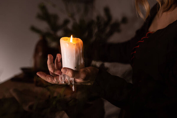 A woman dressed in a medieval dress holds a burning white candle in her hand. Mystery witch