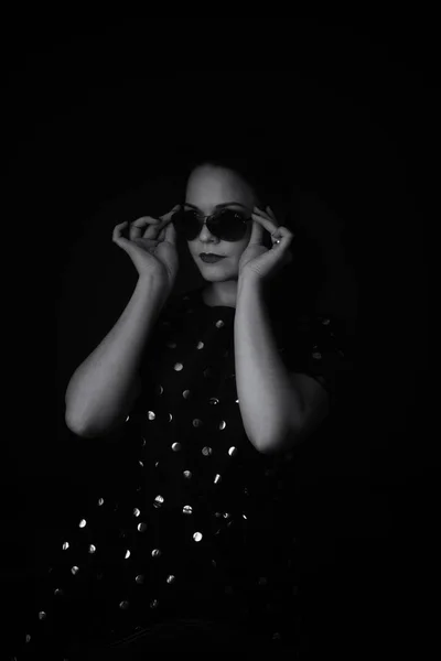 Portret kobiety na rozmytym czarnym tle. Kobieta nosi czarne okulary. czarno-biały obraz. ziarno. — Zdjęcie stockowe