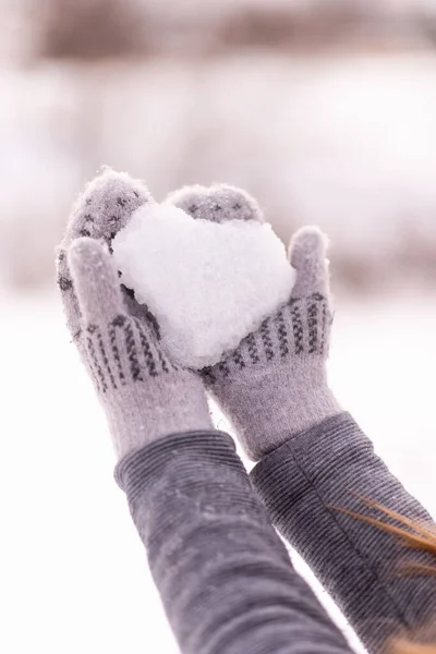 Flicka som håller ett hjärta gjort av snö i händerna. Handskar av grå färg är klädda på händerna. Alla hjärtans dag. — Stockfoto