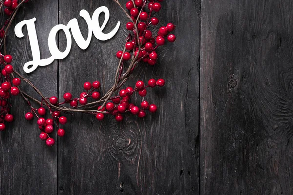 Love - eine Inschrift aus Holz auf dunklem Hintergrund mit roten künstlichen Beeren. — Stockfoto