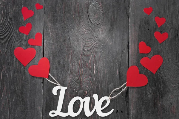 White inscription Love on a dark background with red cardboard hearts as a symbol of Valentine's Day — Stock Photo, Image