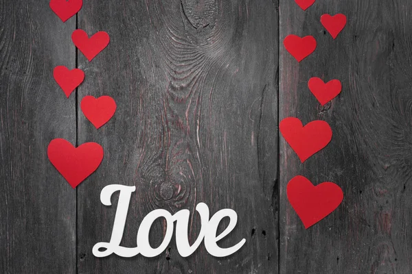Inscrição branca Amor em um fundo escuro com corações de papelão vermelho como um símbolo do Dia dos Namorados — Fotografia de Stock