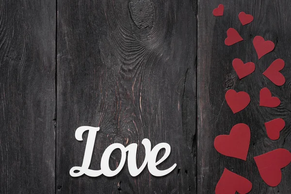 Weißer Schriftzug Liebe auf rustikalem Hintergrund mit roten Pappherzen an der Seite. mit Platz für Text — Stockfoto