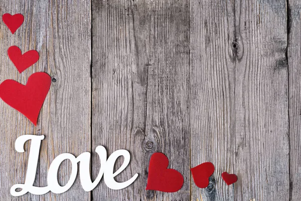 A palavra Amor é escrita em um fundo de madeira cinza ao lado dos corações vermelhos no canto inferior esquerdo da imagem. Foco desligado. Lugar para texto no meio do quadro . — Fotografia de Stock