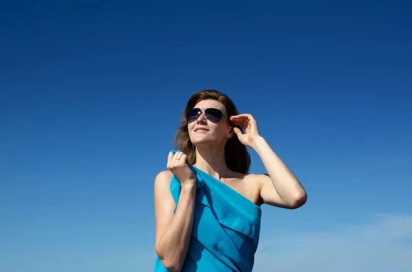 Женщина в солнечных очках на фоне неба смотрит вверх и улыбается. Одетые в голубую одежду — стоковое фото