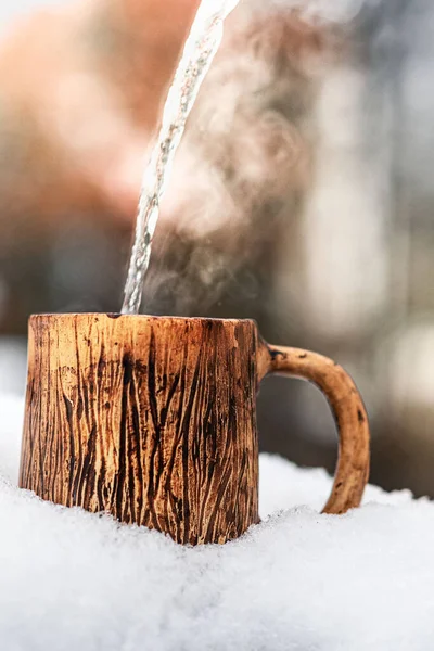 Hot water with steam pours into a clay mug in the snow. outdoors in winter. — Stock Photo, Image