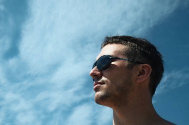 Mavi gökyüzüne karşı güneş gözlüklü vahşi adam yukarı bakıyor. Başarı konsepti.