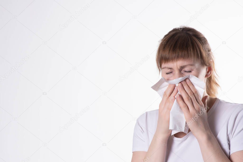 woman in white t-shirt sneezes, covering her nose with a napkin