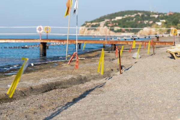 Linha de contorno de fitas amarelas e vermelhas na praia contra o fundo do cais velho — Fotografia de Stock