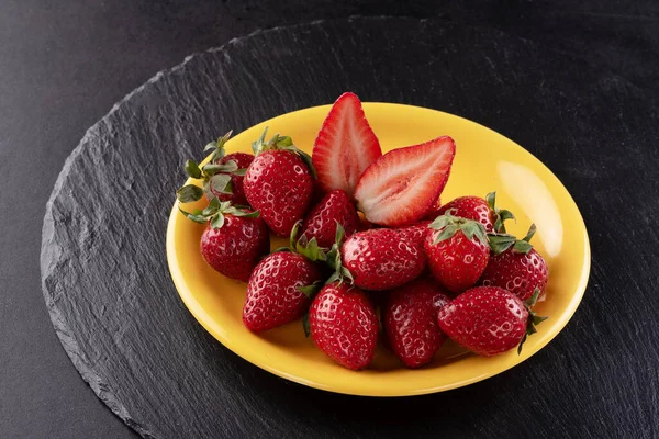 Strawberries on a black background in a yellow plate — Stock Photo, Image