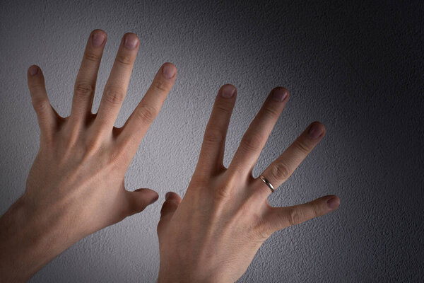 against the background of a gray concrete wall, male hands with spread apart fingers, and a ring on the ring finger