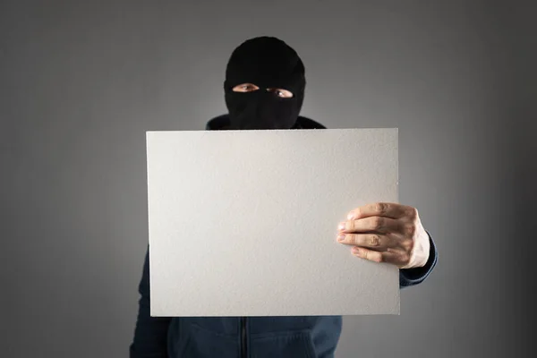 Beväpnad man i en mask på huvudet och med en pistol i händerna håller ett tecken för text — Stockfoto