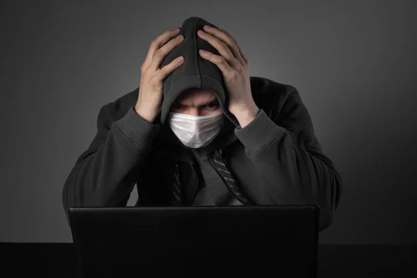 Zamaskowany człowiek za laptopem i w szoku czyta wiadomości o wydarzeniach na świecie i pandemii. — Zdjęcie stockowe