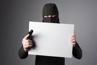 Kar maskeli bir adam beyaz bir tablet tutuyor. Yazacak yeri ve silahı var.