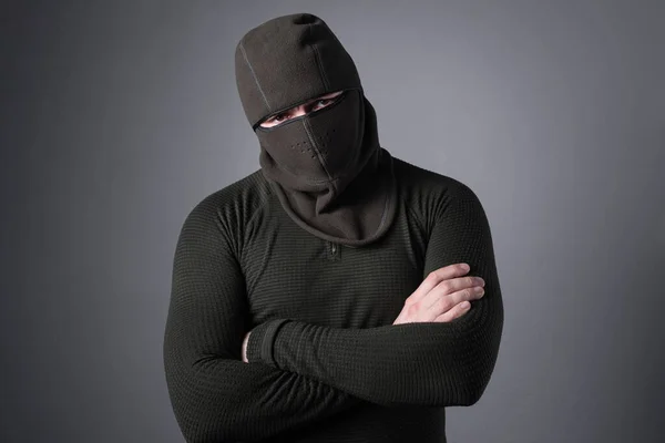 Um homem em uma balaclava, como um conceito de roupas forças especiais, fica com um olhar ameaçador, mãos apertadas em seu peito . — Fotografia de Stock