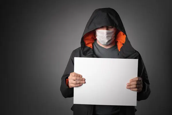 Un uomo in giacca con cappuccio e maschera tiene una tavoletta con un tocco di testo — Foto Stock