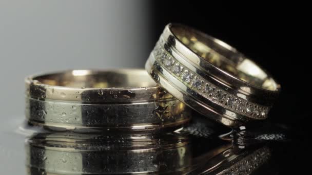 Wedding rings on black and white water surface shining with light. Close up — Stock Video