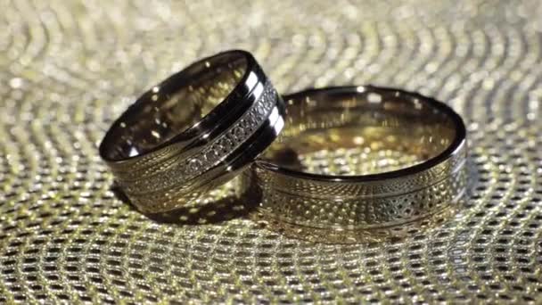 Anéis de ouro do casamento deitado sobre a superfície brilhante brilhante. A brilhar com luz. Close-up — Vídeo de Stock