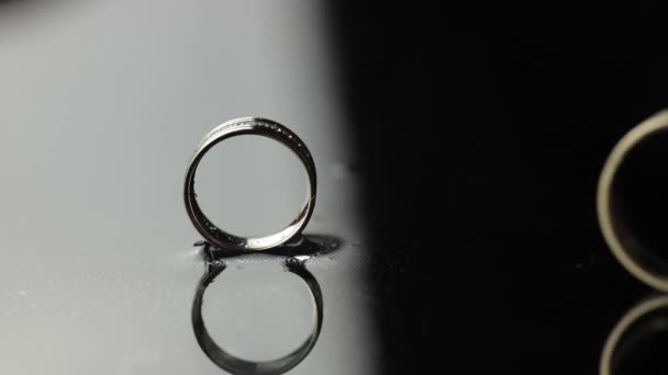 Wedding rings on black, white water surface. Groom ring rolling to brides ring — Stock Video