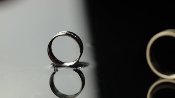 Wedding rings on black, white water surface. Groom ring rolling to brides ring — Stock Video