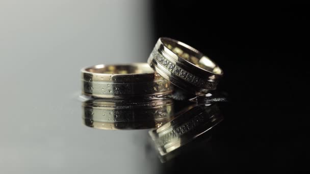 Wedding rings on black and white water surface shining with light. Close up — Stock Video