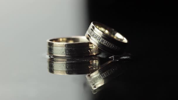 Wedding rings on black and white water surface shining with light. Close up — Stock Video