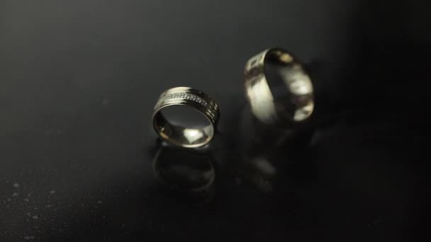 Wedding rings on dark water surface shining with light. One of rings rotates — Stock Video