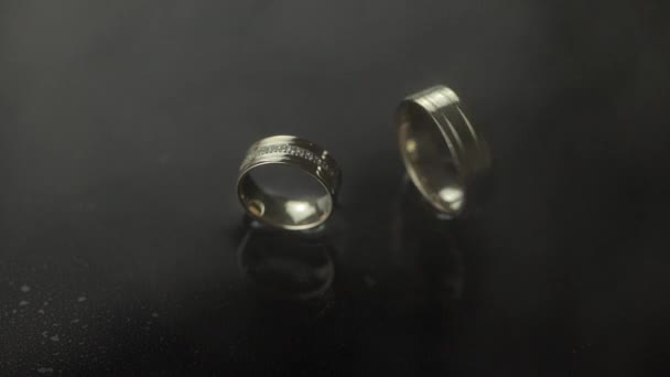 Wedding rings on dark water surface shining with light. One of rings rotates — Stock Video