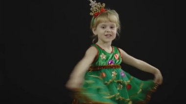 Noel ağacı kostümlü mutlu küçük bir kız bebek. Yüz yap, dans et.