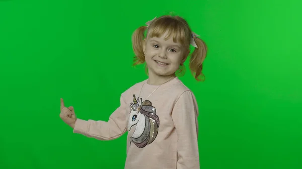 Chica en sudadera unicornio emocionalmente apunta a algo con sus manos —  Fotos de Stock