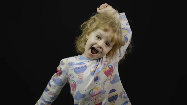 Little baby girl in pajama is fooling around and make faces. Black background — 스톡 사진