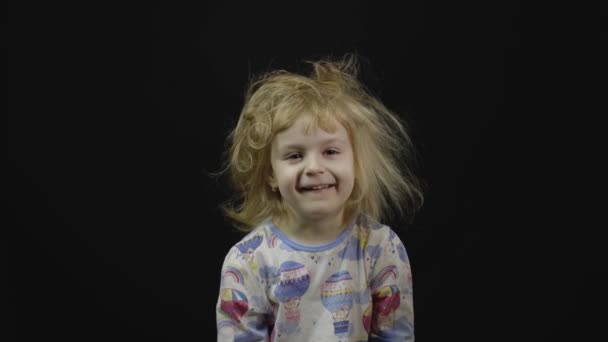 Malá holčička v pyžamu se tu poflakuje a dělá obličeje. Černé pozadí — Stock video