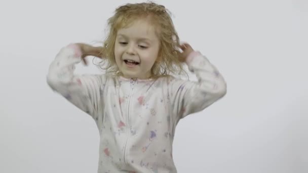 Das kleine Mädchen im Pyjama albert herum und macht Gesichter. weißer Hintergrund — Stockvideo