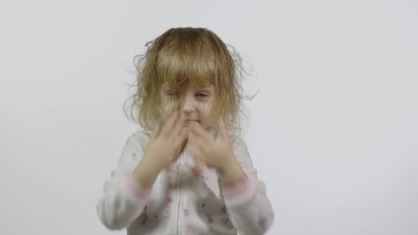 En liten flicka i pyjamas hånglar och gör ansikten. Vit bakgrund — Stockvideo