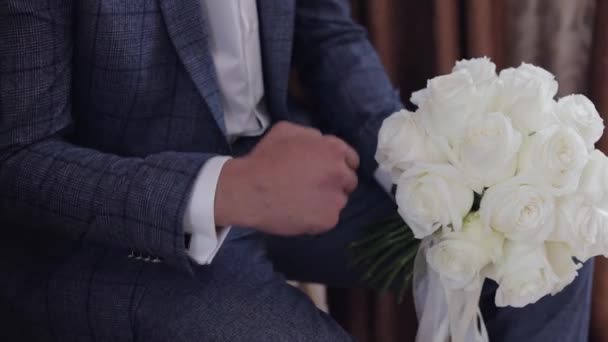 Γαμπρός με γαμήλια ανθοδέσμη στα χέρια του στο σπίτι. Λευκό πουκάμισο, σακάκι — Αρχείο Βίντεο