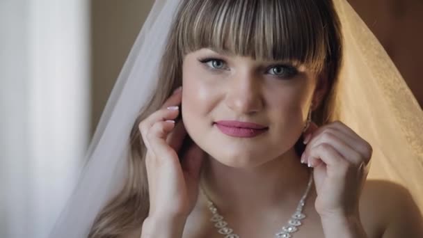 Beautiful and lovely bride in wedding dress and veil puts on earrings — 비디오