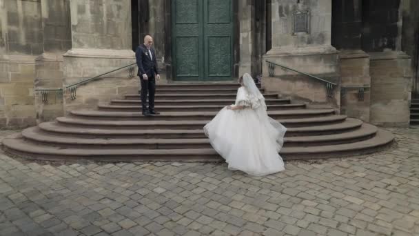 Прекрасная невеста идет к жениху на древней лестнице рядом с церковью — стоковое видео