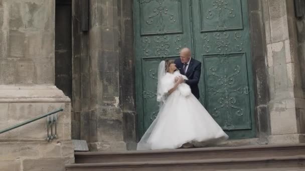 Прекрасная невеста и жених на старинной лестнице рядом с церковью — стоковое видео
