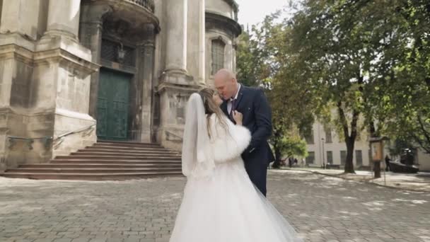 Recién casados en el centro de la ciudad. Novia y novio cerca de la iglesia antigua — Vídeo de stock