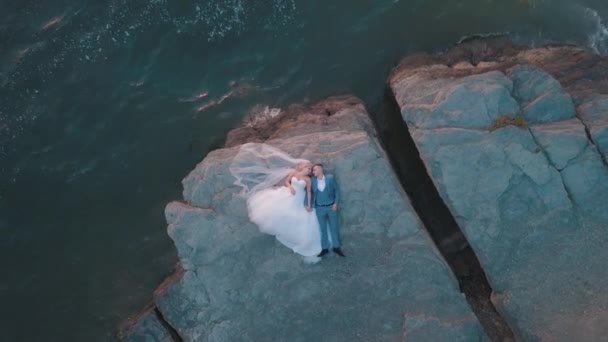 Bröllop nygifta par ligger på en bergssida vid havet. Flygskott — Stockvideo
