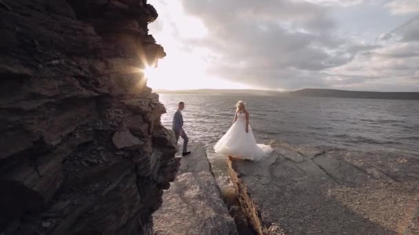 Brudgummen går till bruden och hjälper henne. Nygifta på bergssidan vid havet — Stockvideo