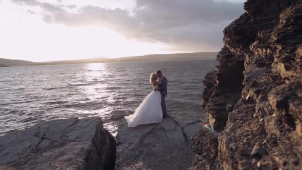 Das frisch vermählte Paar an einem Berghang am Meer. Sonnenuntergang. Bräutigam und Braut — Stockvideo