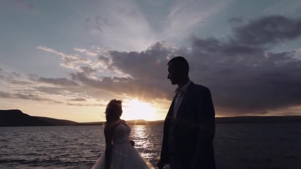 Nygifta par på en bergssida vid havet. Solnedgång. Brudgum och brud — Stockvideo
