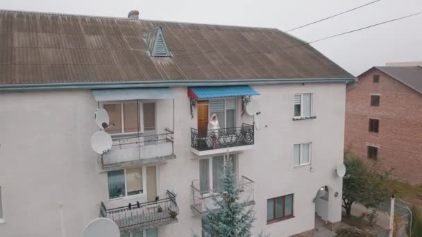 Sposa in abito da notte stand sul balcone della sua casa. La mattina del matrimonio. Vista aerea — Video Stock