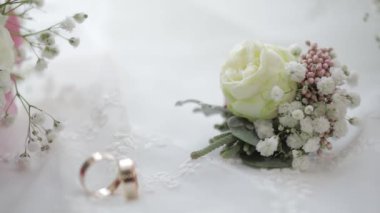 Beautiful wedding bouquets lie with wedding rings near window on white curtains