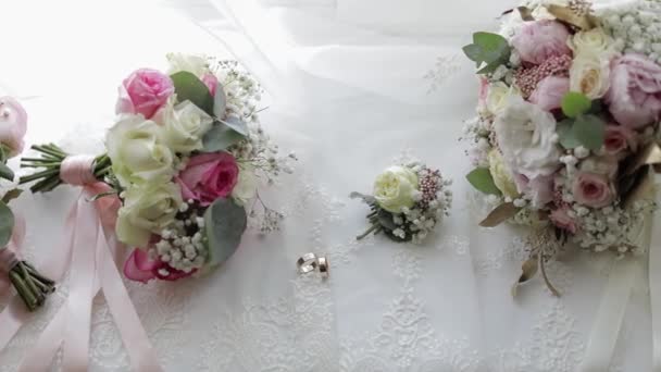 Beautiful wedding bouquets lie with wedding rings near window on white curtains — Stockvideo