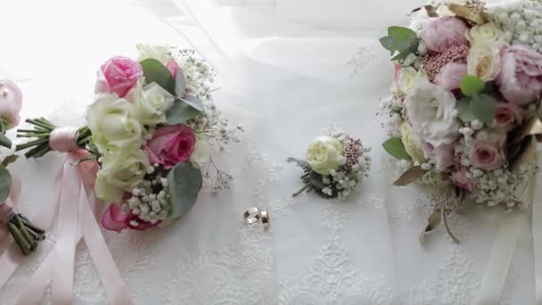 Beautiful wedding bouquets lie with wedding rings near window on white curtains