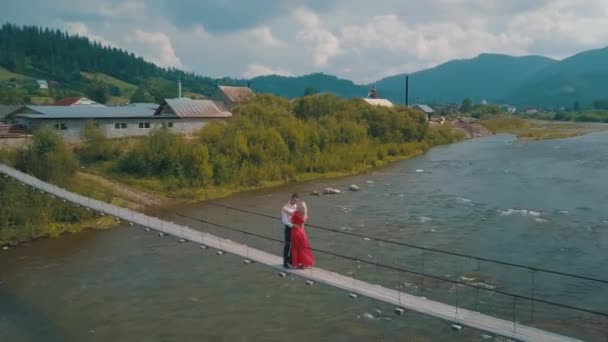 Pareja se encuentra en el puente sobre un río de montaña. Amor al hombre y a la mujer — Vídeo de stock